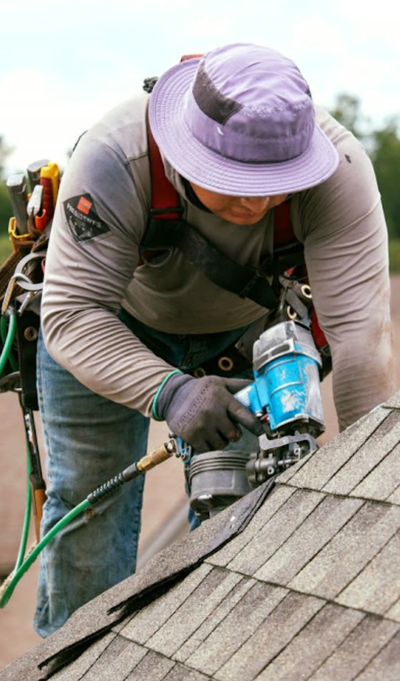 Roofer installing shingles with a nail gun